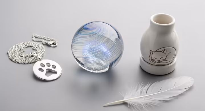 A collection of modern pet memorial items, including a glass art piece with ashes, a pendant, and a decorative urn.